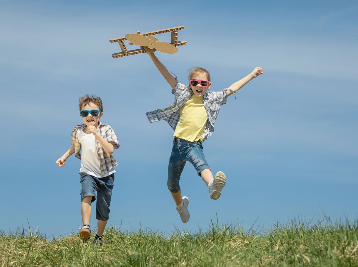 Ein Junge und ein Mädchen spielen mit einem Propellerflugzeug aus Karton